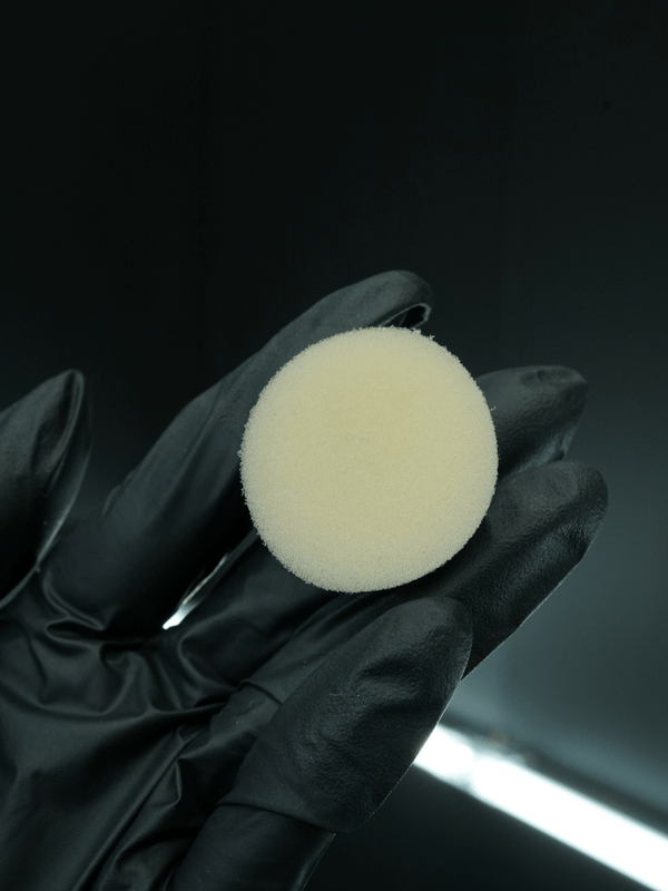 Black glove holding a white buffing pad against a dark background
