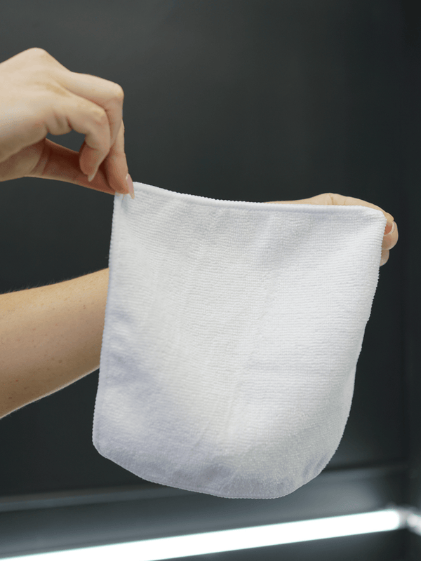 Small white microfibre cloth held by a hand against a dark background