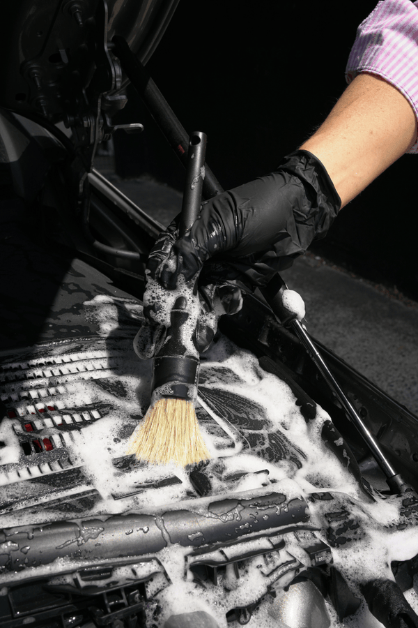 Person cleaning a car's bonnet with a brush and soapy water.