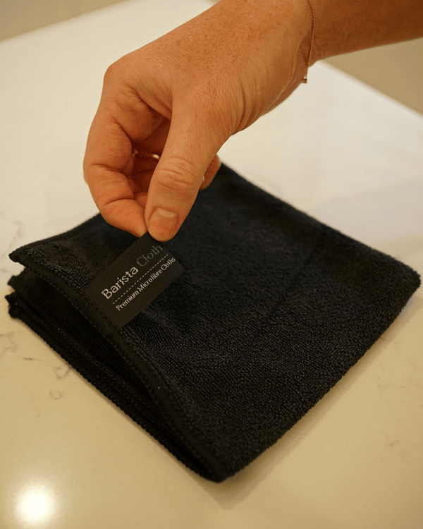 Hand holding a black towel with a brand label on a light surface
