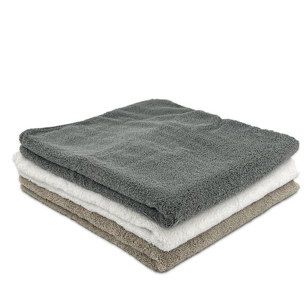 A stack of three microfibre bath towels in grey, white, and beige colours.