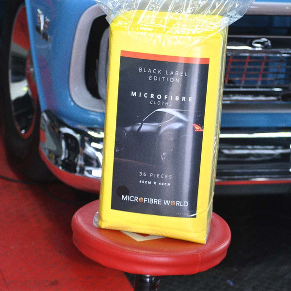 A packet of yellow microfibre cloths sitting on a re stool in front of a blue car