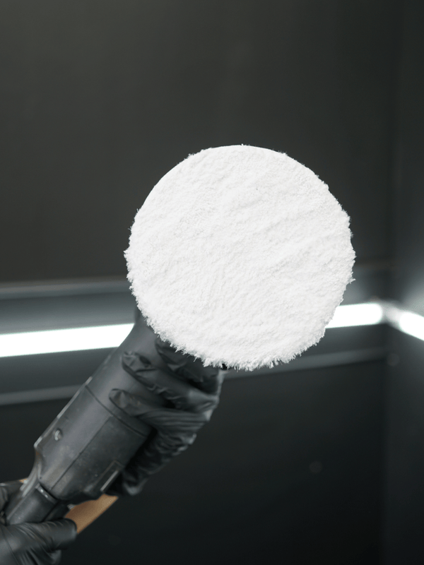 Buffing machine with a white foam cover held by a person wearing black gloves against a dark background