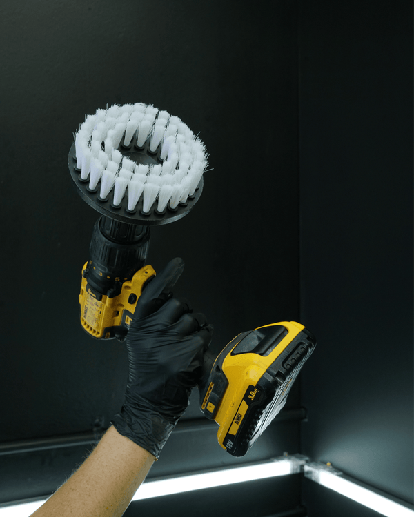 A person wearing black gloves holding a drill with a carpet drill brush attached
