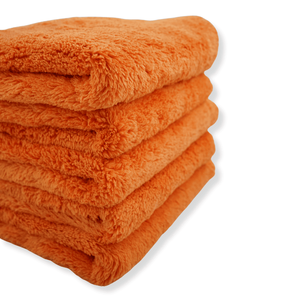 A close up of a stack of ultra plush orange microfibre cloths on a white background