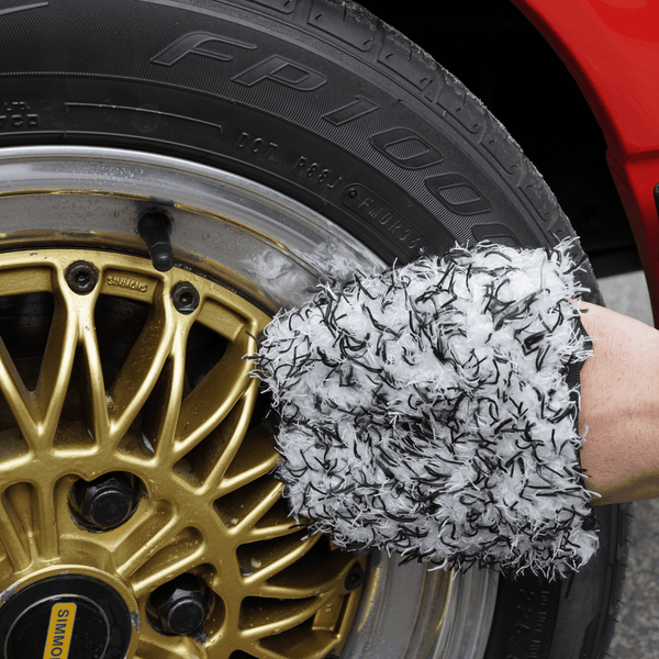 Person cleaning gold wheel with black and white wheel mitt