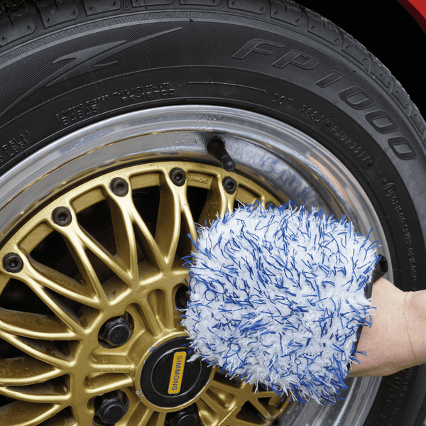 Person cleaning gold wheel with blue and white wheel mitt