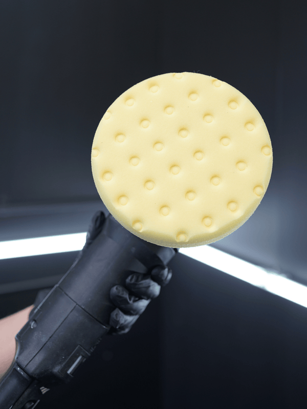 Polishing tool with a yellow pad held against a dark background