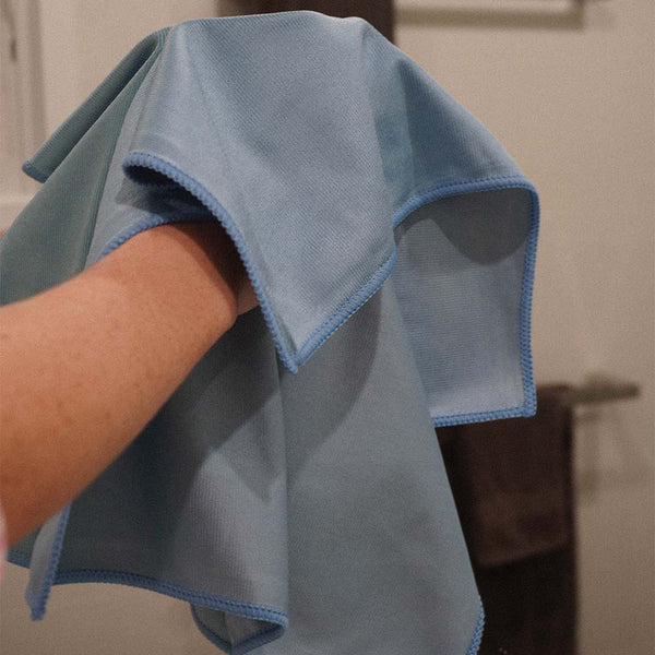 A person cleaning a mirror with a blue glass cloth
