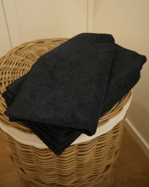 Black towel folded on top a wicker laundry basket against a neutral wall.