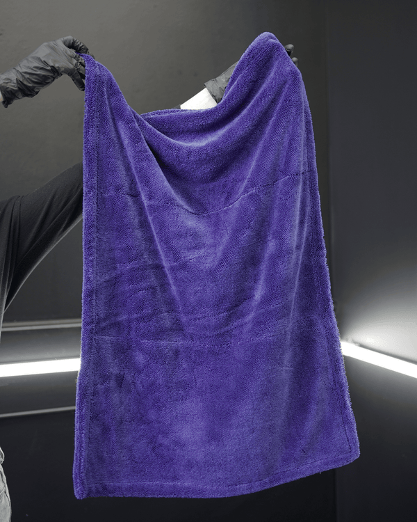 A person wearing black gloves holding a large blue microfibre drying towel in a detailing bay