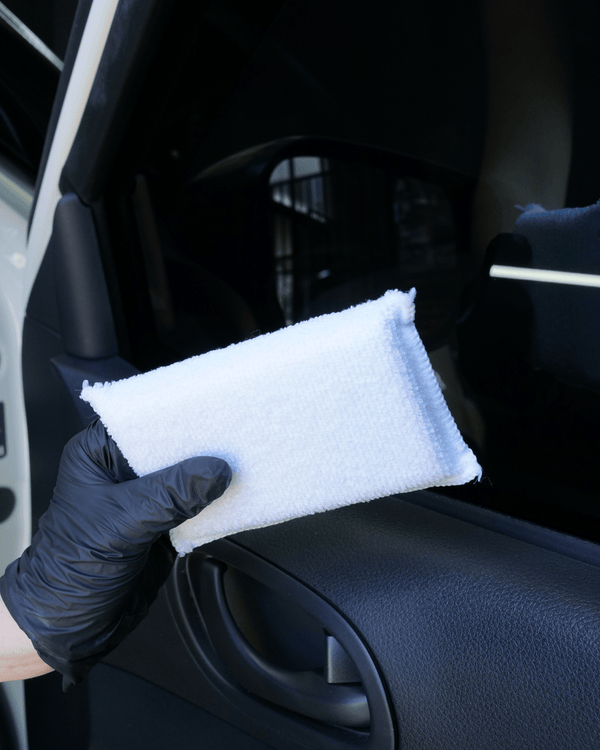A person wearing black gloves holding a white interior applicator in front of a car door