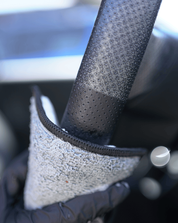 A person cleaning a dirty steering wheel with a microfibre interior scrub sponge