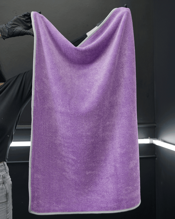 A person wearing black gloves holding a large purple microfibre drying towel in a detailing bay