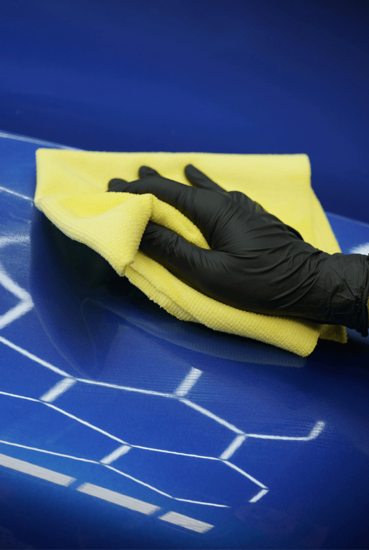 Hand wearing a black glove cleaning a blue car with a yellow microfibre cloth