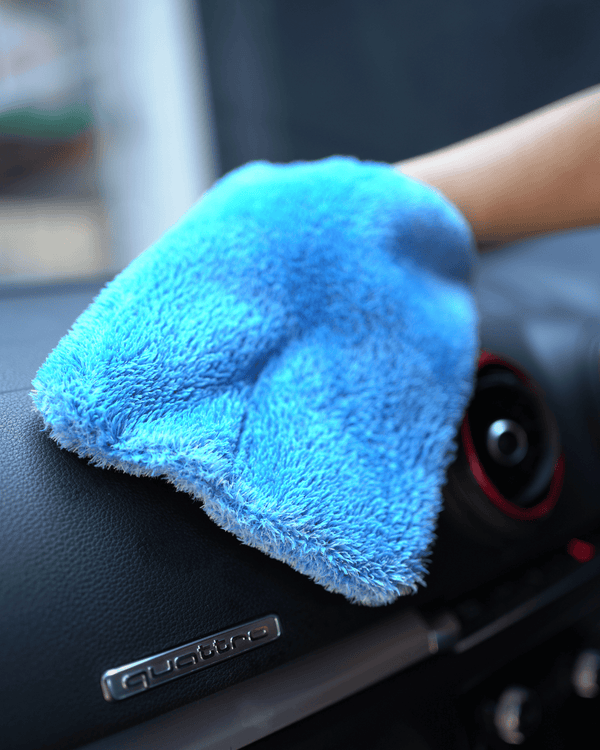 A person holding a blue interior scrub mitt cleaning a car dashboard