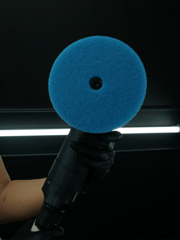 Blue foam buffer held by a gloved hand against a dark background