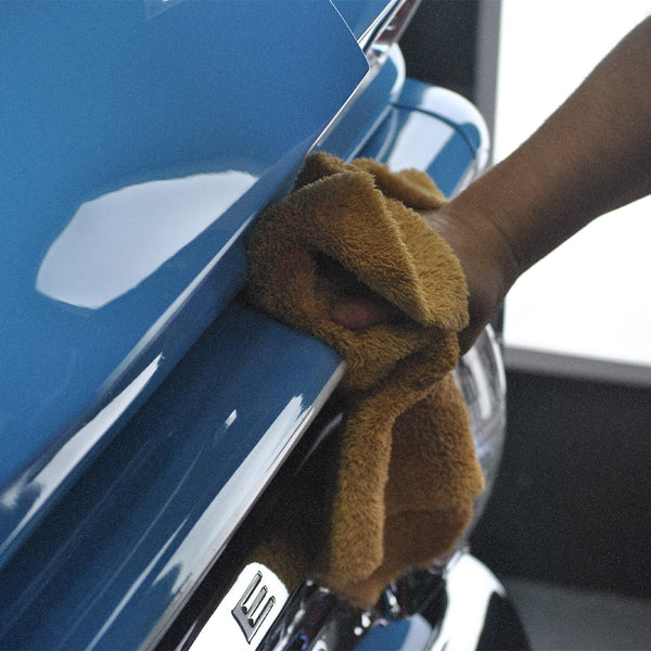 A person wiping a car with a plush orange microfibre cloth