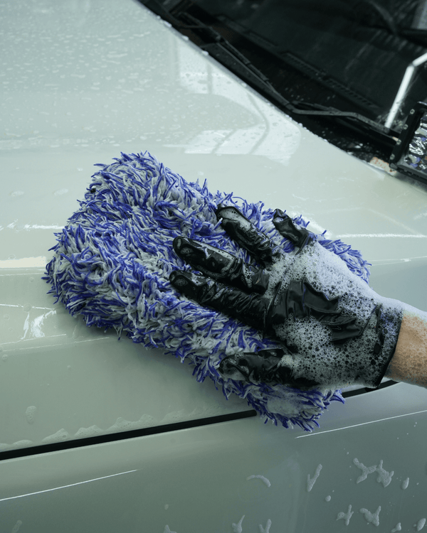A person wearing black gloves holding a blue and white microfibre car wash mitt