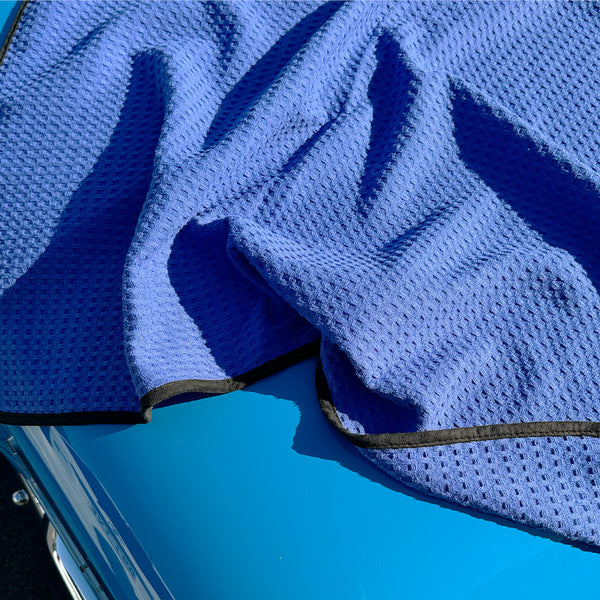 A dark blue waffle weave microfibre drying towel spread over a car bonnet