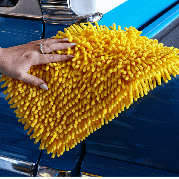 Person cleaning a blue car with a yellow microfiber cloth