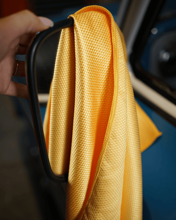 Person cleaning a car mirror with a yellow microfiber cloth.