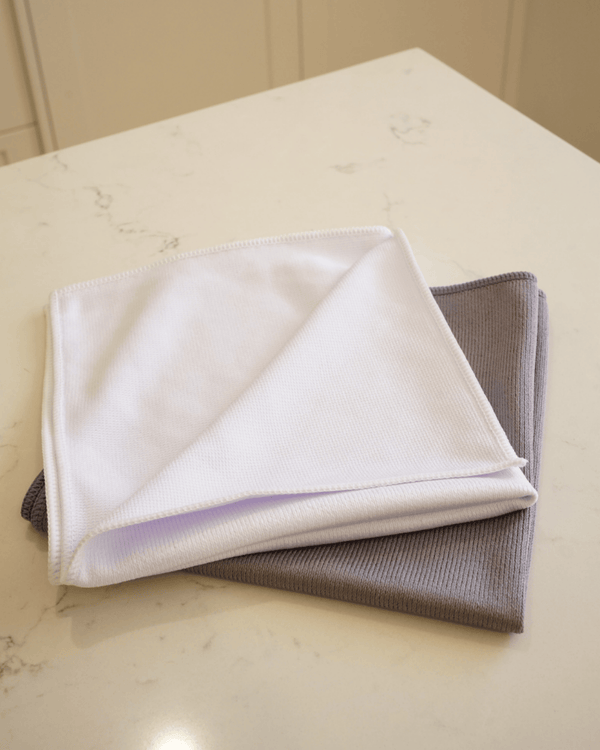 Two folded microfibre glass cloths, one white and one grey, on a marble surface.