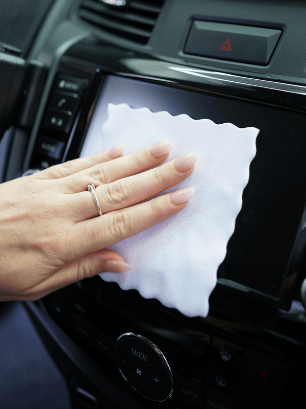 Person cleaning a car's dashboard with a white suede cloth.