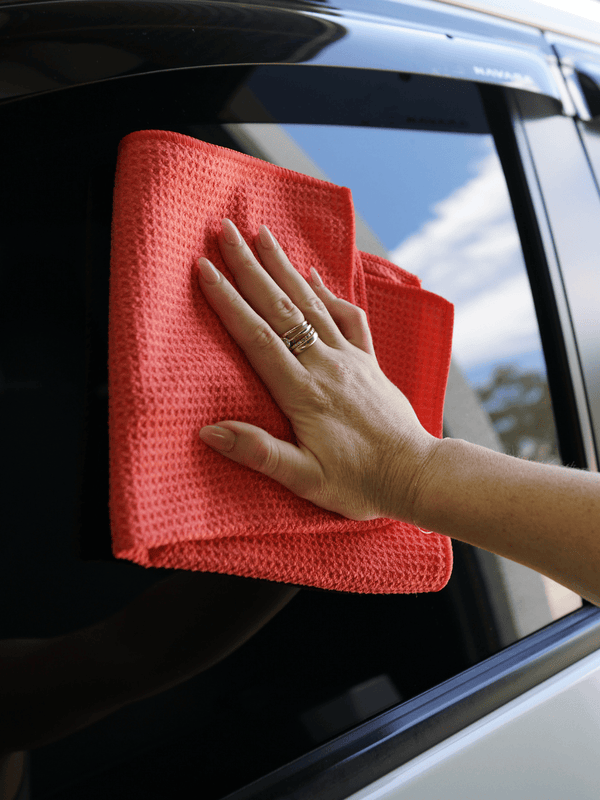 Person cleaning a car window with a red microfibre cloth