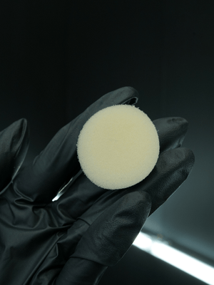 Black glove holding a white buffing pad against a dark background