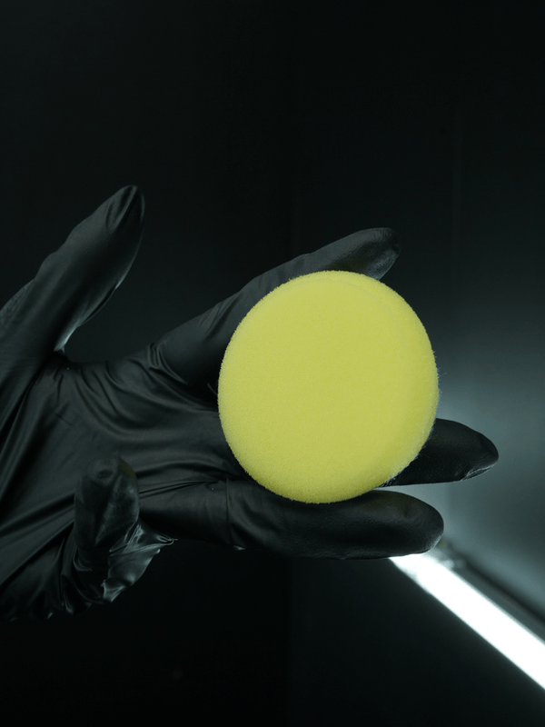 Black glove holding a yellow buffing pad against a dark background