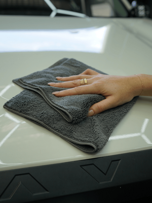 Person's hand holding a grey towel on a car surface