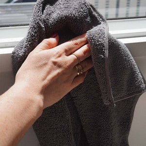 A person using a grey microfibre cloth to clean a window