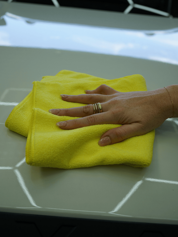 Hand with a ring holding a yellow cloth on a light grey surface