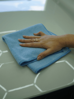 Hand with a ring holding a blue microfibre cloth on a white surface