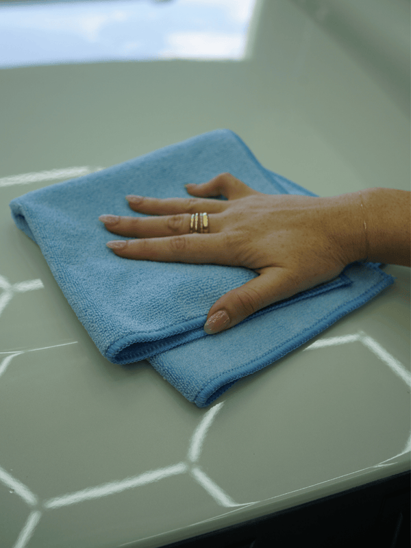 Hand with a ring holding a blue microfibre cloth on a white surface