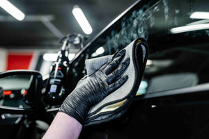 Person in black glove cleaning a car window with the grey and yellow ADBL Yellowstone glass towel