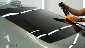 Detailer cleaning or sealing car rear window with spray product and orange microfibre cloth