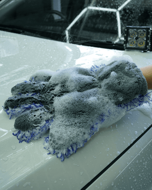 A person cleaning a white car with a 5 finger microfibre wash mitt