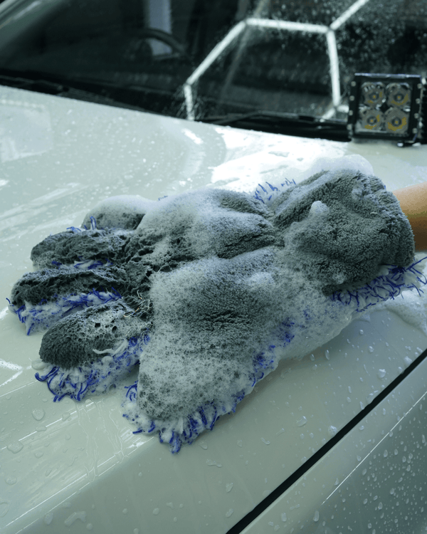 A person cleaning a white car with a 5 finger microfibre wash mitt