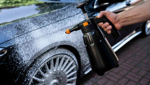 A person holding a black foam spray bottle using it to clean a black car