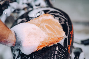 A person cleaning a motorbike with a soapy orange microfibre wash mitt