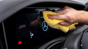 A person wiping a car dash with a yellow microfibre cloth