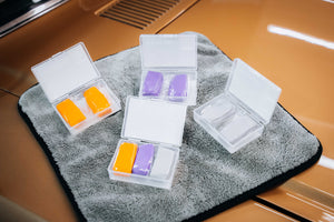 4 open boxes of clay bars in different colours on a plush microfibre coth on a car bonnet