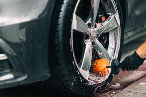 Close-up of person cleaning a dirty car wheel and tire with the ADBL Wheel Sword brush and pink wheel cleaner
