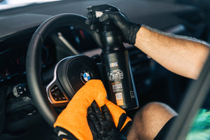 Person cleaning BMW steering wheel with ADBL Interior Cleaner and an orange microfibre towel