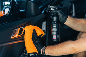 Person in black glove spraying ADBL INTERIOR QD onto a car door panel handle and interior surfaces