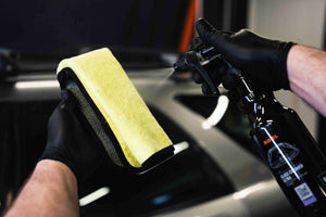 Person in black gloves spraying glass cleaner onto an ADBL Yellowstone microfibere glass towel before use