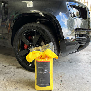A packet of yellow cloths open at the top sitting on the floor in front of a car wheel