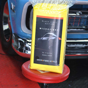 A packet of yellow microfibre cloths sitting on a re stool in front of a blue car
